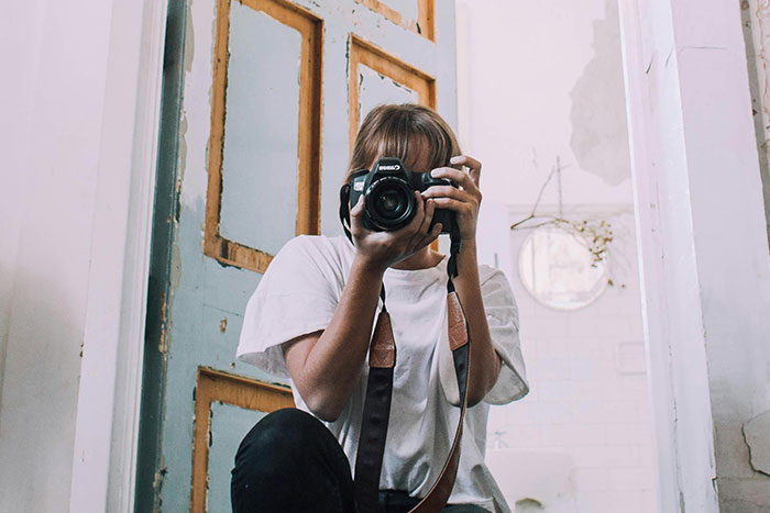 Woman with a camera taking a picture in a rustic, vintage interior setting.