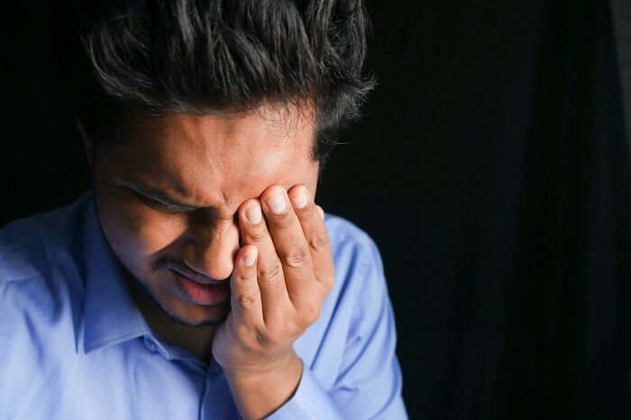 Man in a blue shirt touching his face, possibly experiencing discomfort related to rare cosmetic procedures.