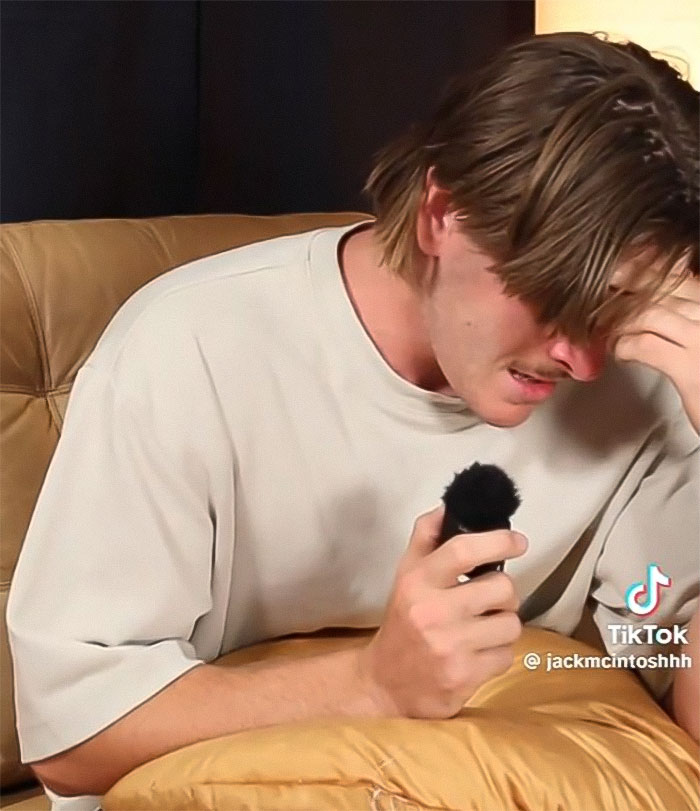 Podcaster tearfully reacts during a discussion, holding a microphone, highlighting "Not All Men" theme.