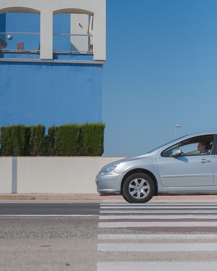 Silver car aligned with a blue building, creating a visual coincidence, by Denis Cherim.