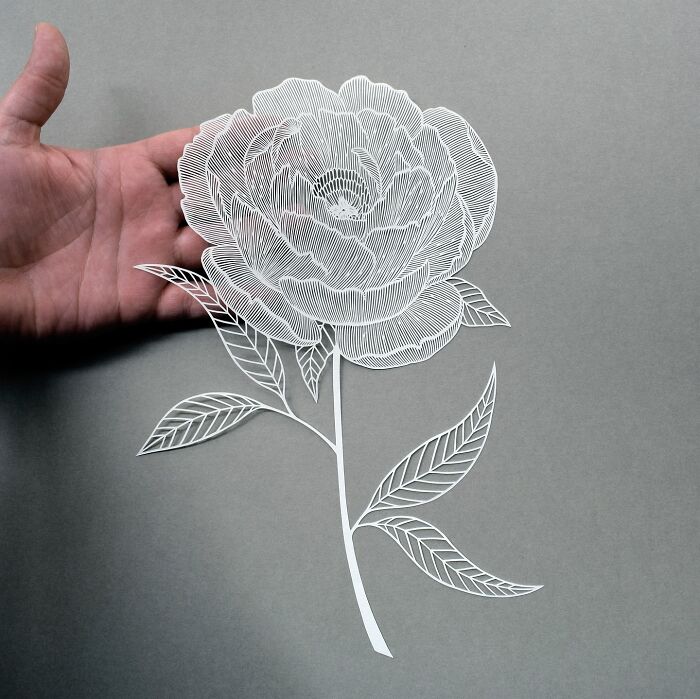 Intricate paper art design of a delicate flower held by a hand, inspired by nature.