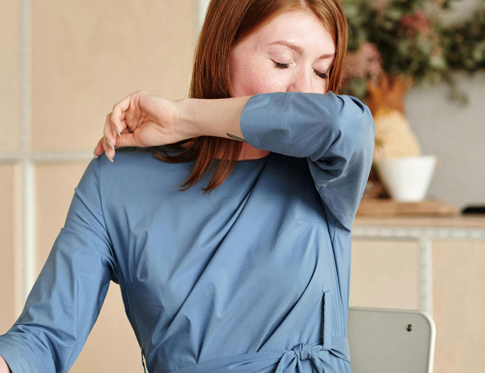 Estudiante sonriendo y cubriendo su rostro con el brazo en un aula, destacando momentos graciosos en clase.