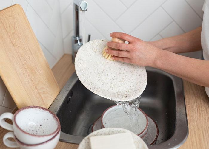 A woman adds whimsy to life by washing dishes with a handmade brush, creating a serene kitchen moment.