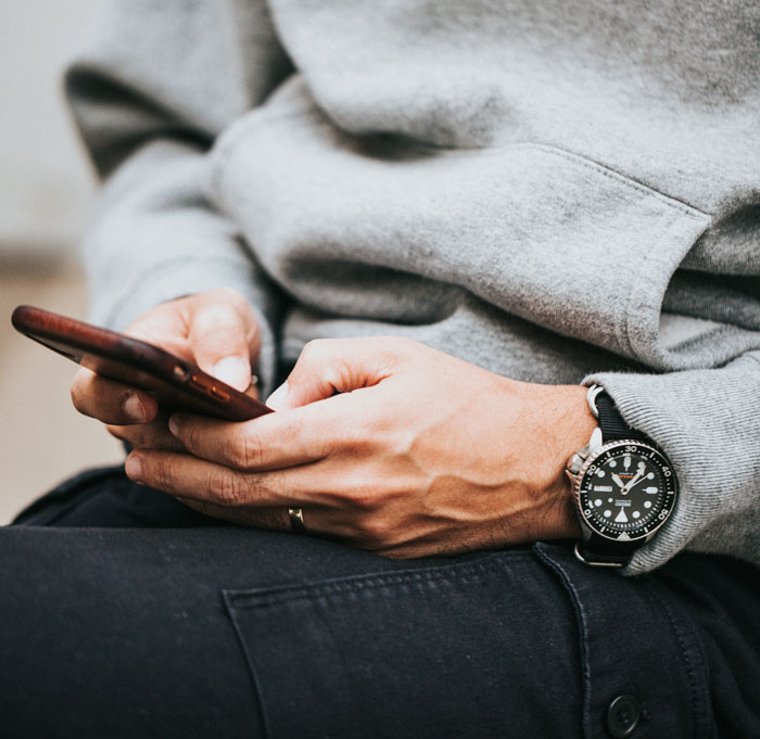 Person in a grey sweater holding a phone, focusing on a wristwatch. Vegan family dynamics concept. Person in a grey sweater holding a phone, focusing on a wristwatch. Vegan family dynamics concept.