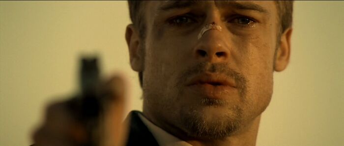 A person with a bruised face holding a gun, representing celebrities in the 90s in a dramatic scene.