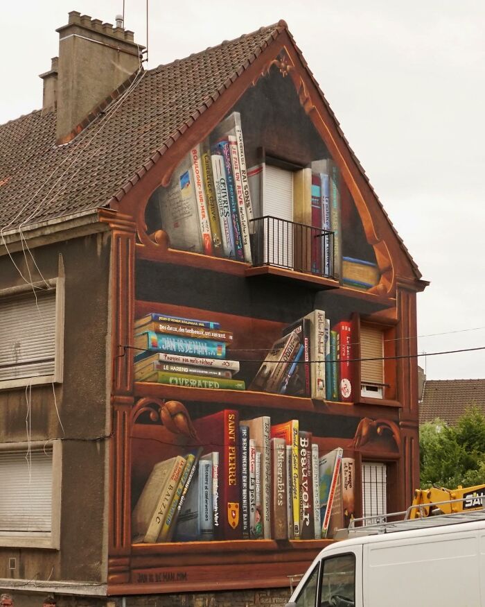 Hyperrealistic mural by Jan Is De Man on city wall, depicting a bookshelf illusion with detailed books.