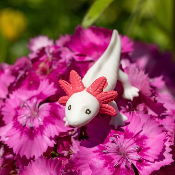 Cute Archie McPhee axolotl toy resting on bright pink flowers in sunlight.
