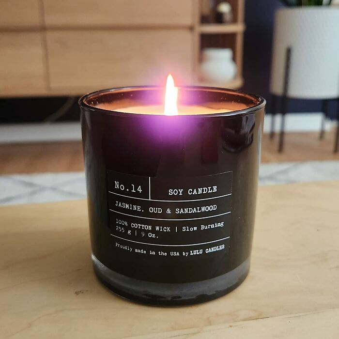 Black soy candle with jasmine, oud, and sandalwood scent burning on a wooden surface, showing expensive taste on a humble budget.