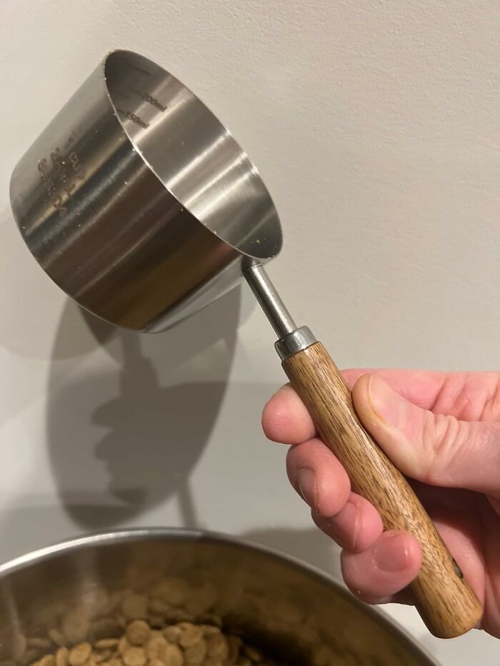 A hand holding a measuring cup with a wooden handle, showcasing a practical impulse buy.