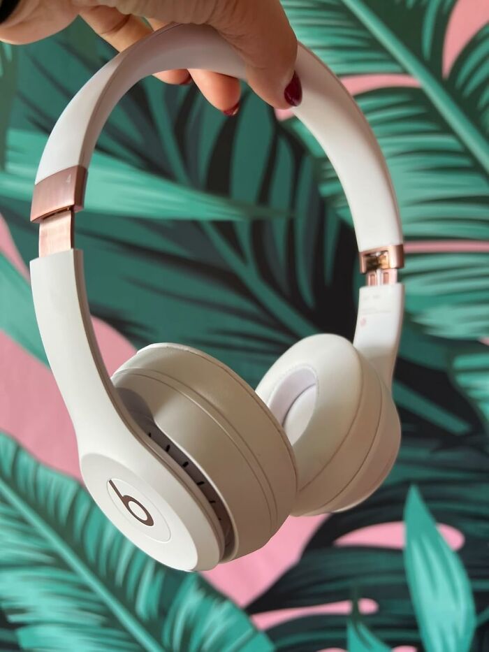 White over-ear headphones held against a leafy background, emphasizing work from home tech essentials.