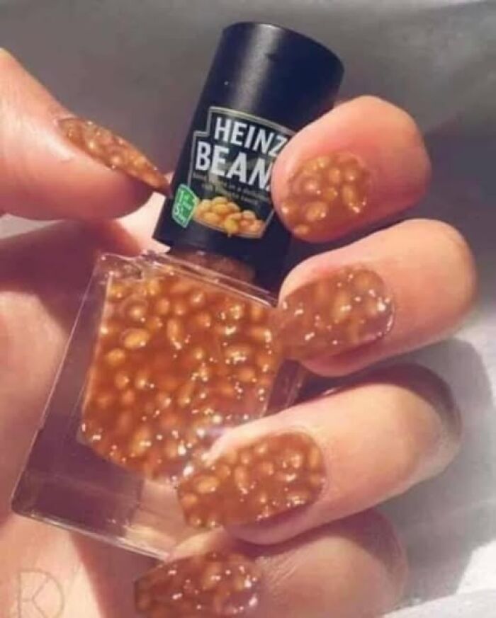 Weird image of nails painted to look like baked beans, holding a Heinz Beans nail polish bottle.