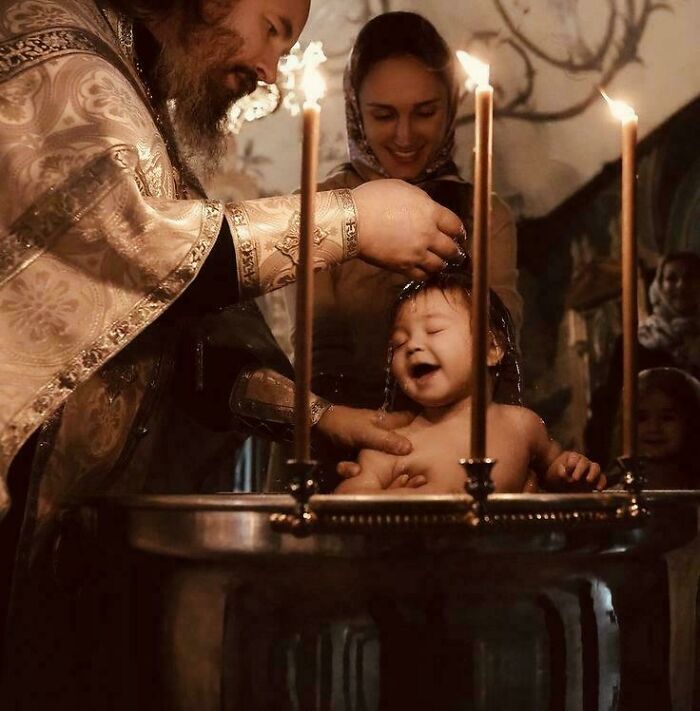 Priest baptizing a joyful child, illuminated by candlelight, exuding an accidental Renaissance painting vibe.