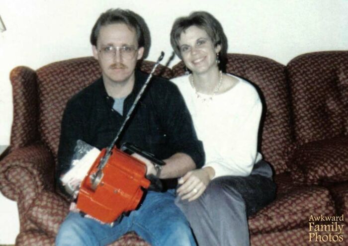 Man and woman sitting on a couch holding a chainsaw, an awkward family photo that feels incredibly sweet and genuine.