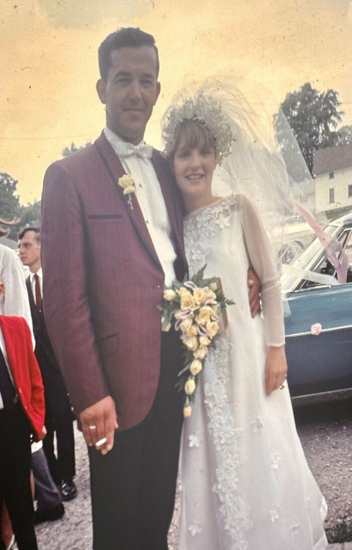 Vintage wedding photo featuring a smiling couple in formal attire, groom in maroon jacket, bride in white gown.