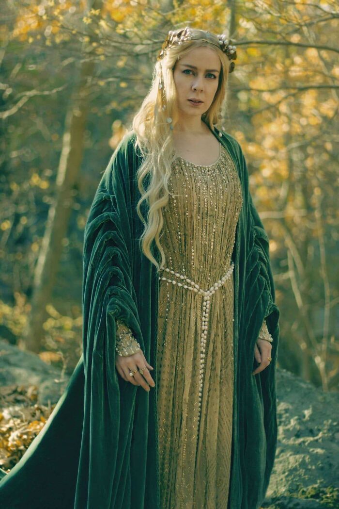 Woman in an elaborate DIY dress and cape, standing in a forest setting with autumn leaves.