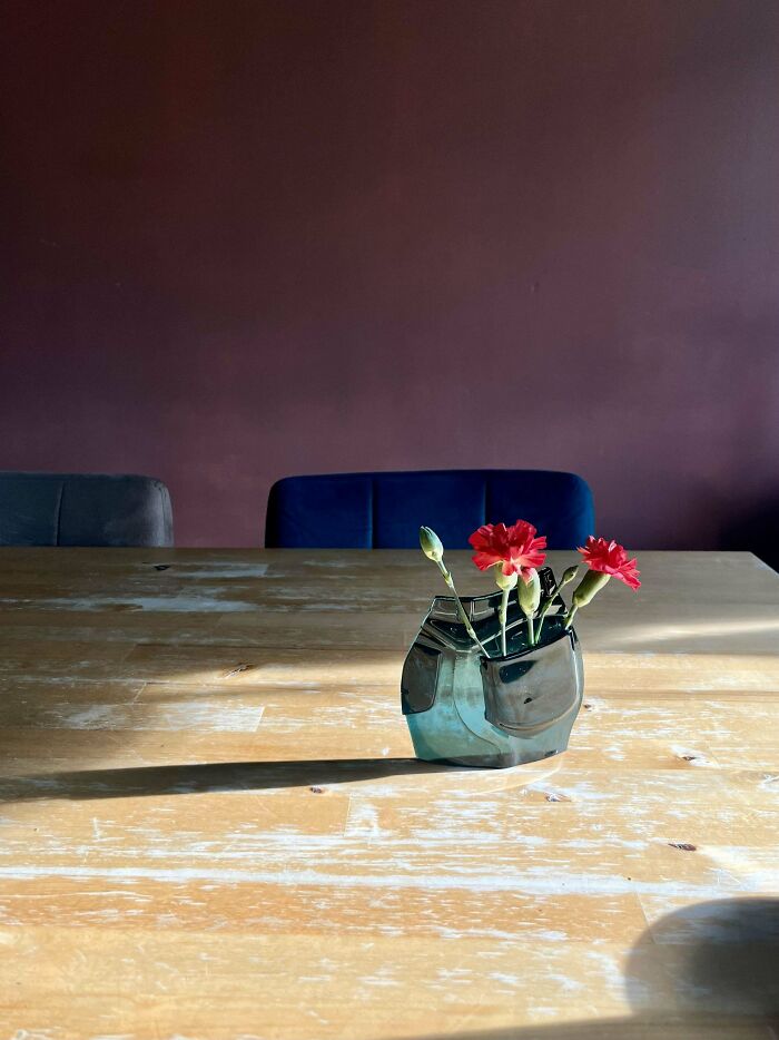 DIY project with red flowers in a unique, angular vase on a wooden table against a maroon wall.