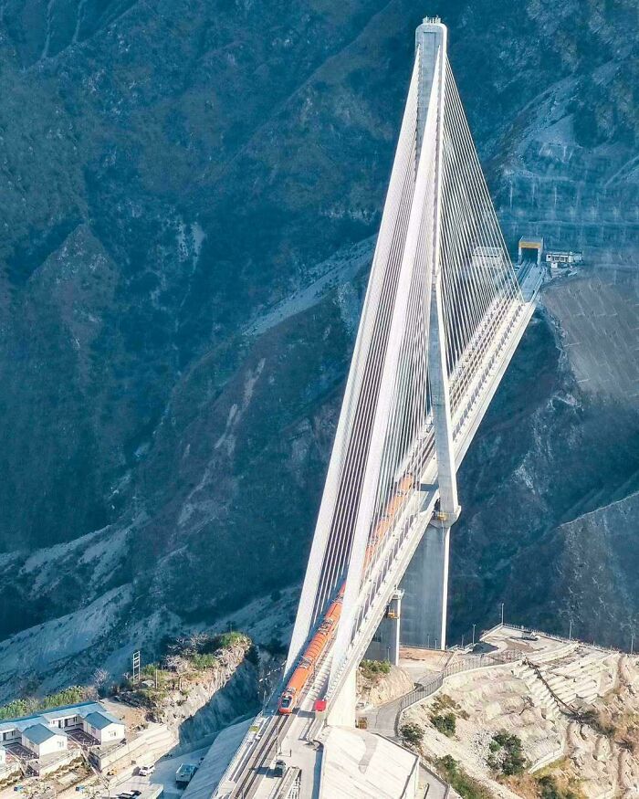Cable-stayed bridge with a train crossing, showcasing brilliant infrastructure against a mountainous backdrop.