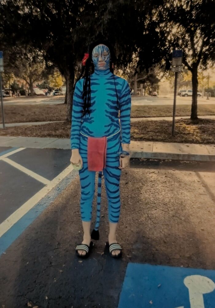 Person in a cringe-worthy regrettable past costume resembling a blue striped creature standing in a parking lot outdoors.