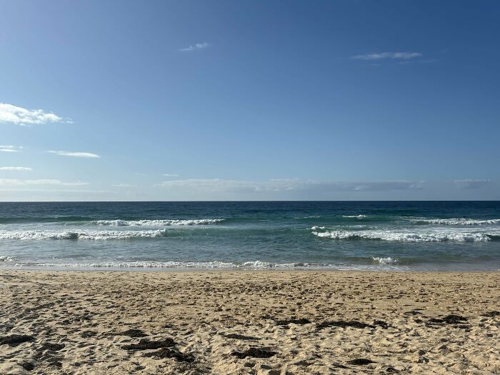 Sandy beach with gentle waves under a clear blue sky in Australia.