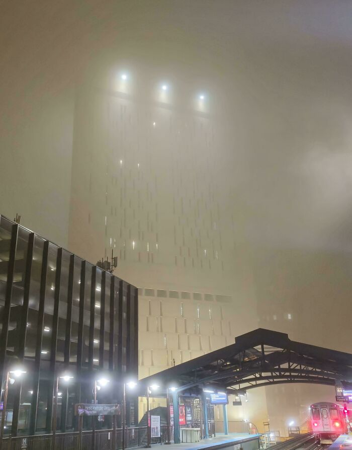 Tall building with an eerie glow and fog creating a supervillain headquarters vibe at a dimly lit train station.