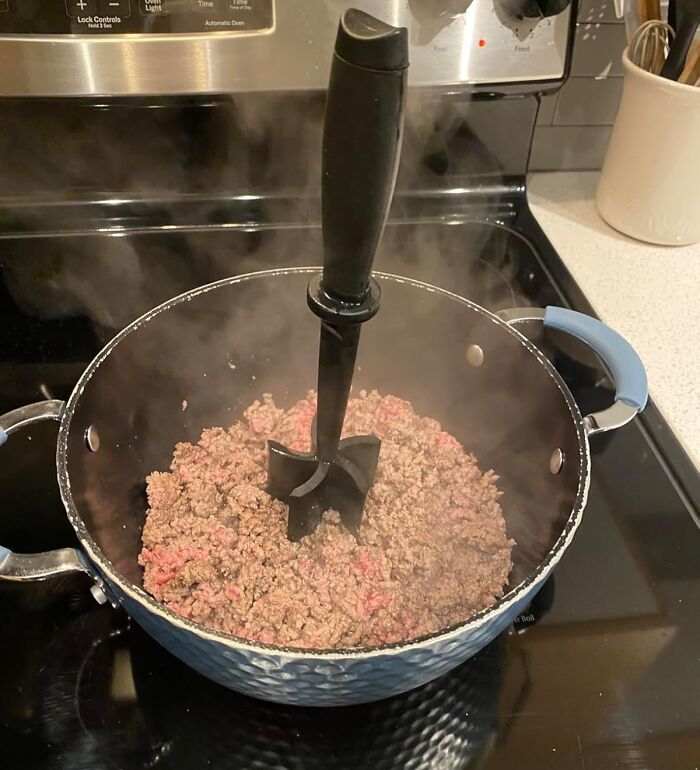 Meat masher in use, chopping ground meat in a pot on the stove, highlighting kitchen tools worth spending money on.