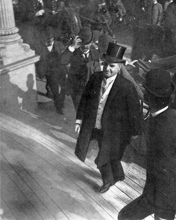 A group of men in formal attire and top hats ascend steps in a rare historical photo.
