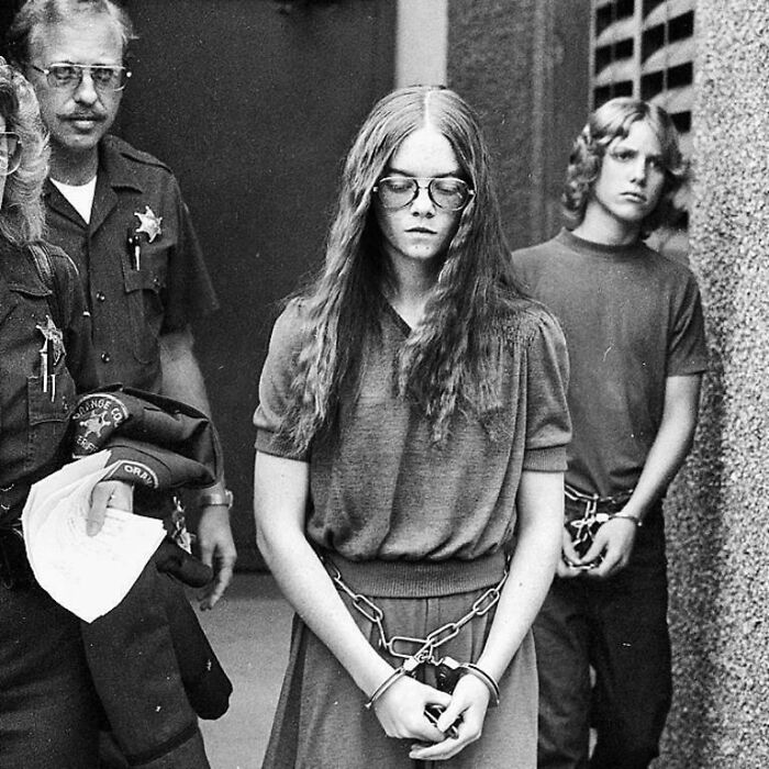A historical photo depicts a young woman in handcuffs escorted by officers, providing a rare view of past events.