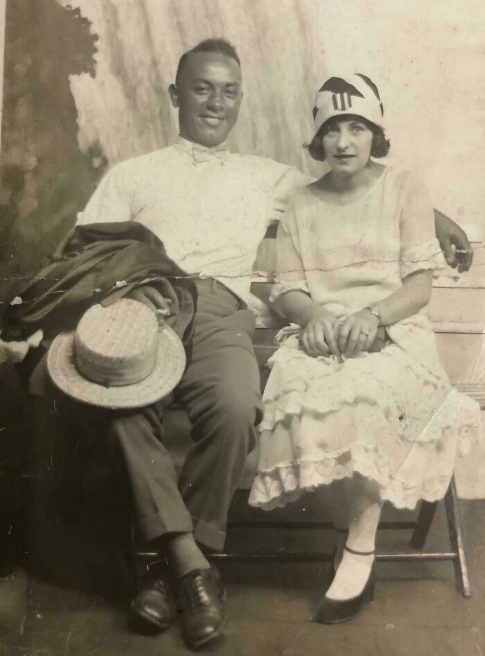 Rare historical photo of a smiling couple sitting on a bench, the man holding a straw hat, and the woman wearing a stylish cloche hat.