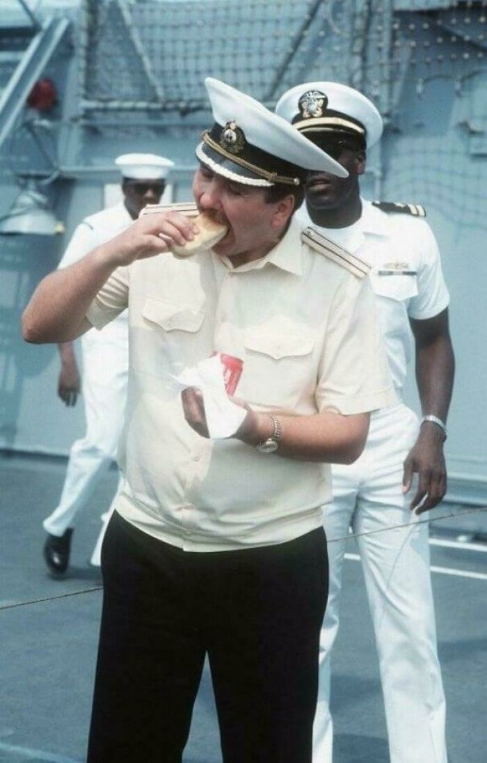 Navy officers in uniform on a ship, one eating a sandwich, a rare historical photo capturing a candid moment.