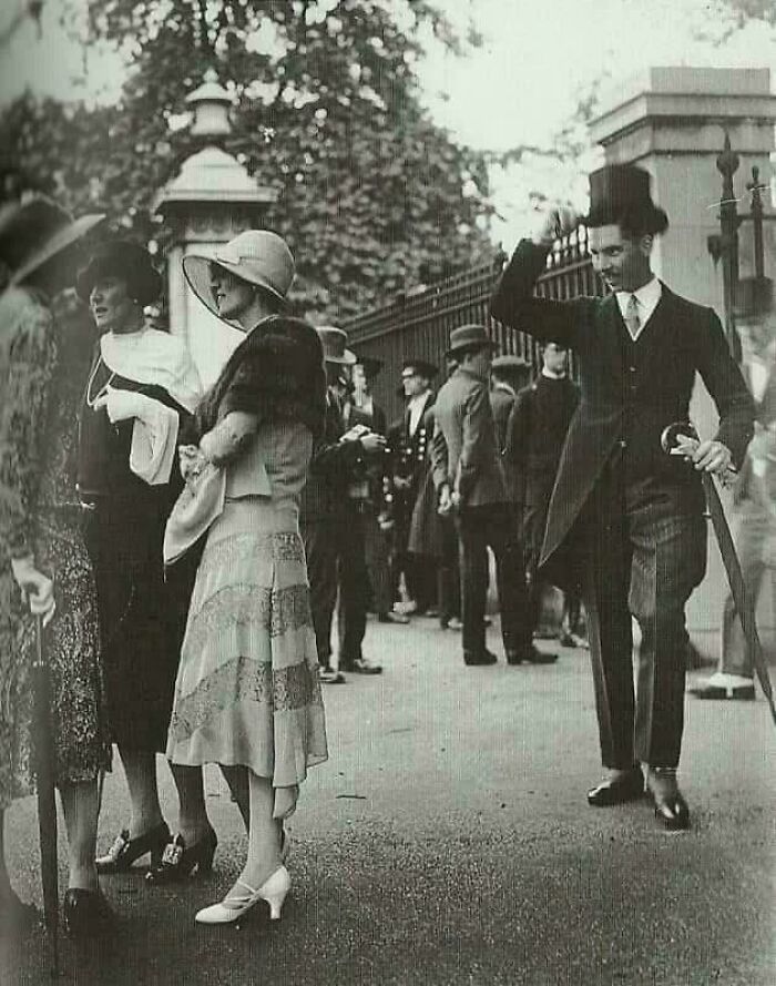 Historical photo showing elegantly dressed people in early 20th-century fashion, with a man tipping his hat.