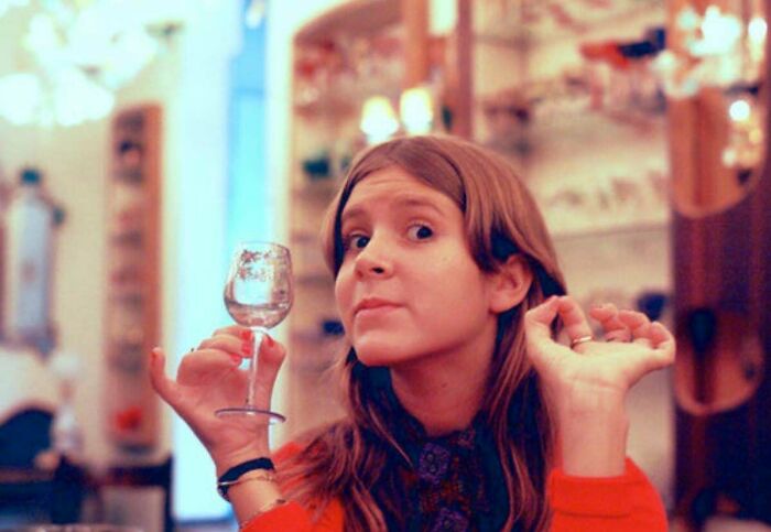 A woman in a vintage setting holds a small glass, embodying rare historical moments with a playful expression.