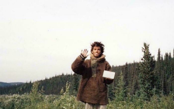 A man in a rustic coat waves in a forest, holding an item, illustrating a rare historical moment.