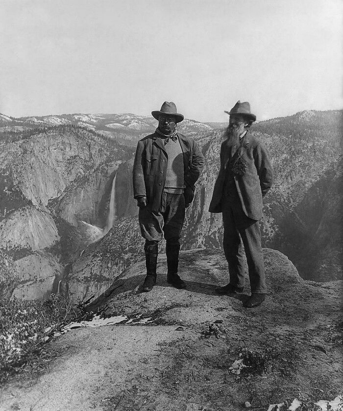 Two men in 1900s attire stand on a cliff with a waterfall in background, representing rare historical photos.