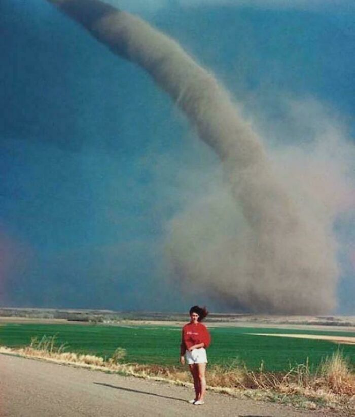 A woman stands on a rural road with a large tornado in the background, illustrating a rare historical weather event.