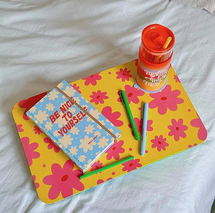 Bando products: floral tray, journal, pens, and tumbler on a bed.