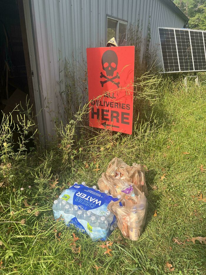 Instacart shopper delivery left by a red warning sign with a skull, on grassy ground near a building with solar panels.