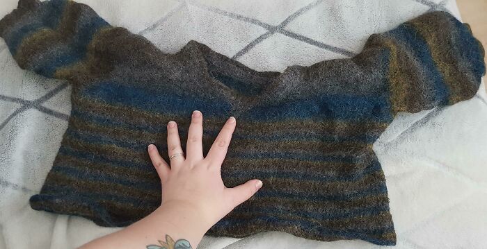A hand touches a shrunken striped sweater, showcasing hilarious misunderstandings of laundry mishaps.