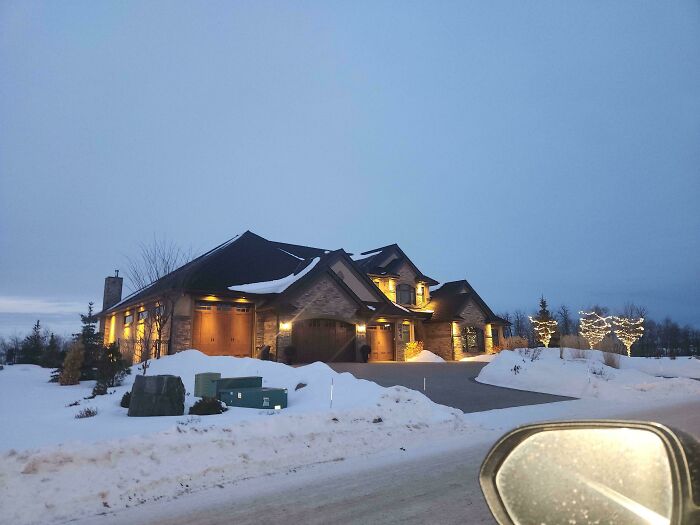 Luxurious snowy mansion at dusk with car mirror visible, Instacart shopper's unique delivery destination.