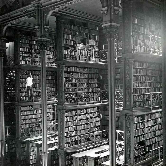 Historical photo of a vast library with towering bookshelves and a solitary person amidst the volumes.