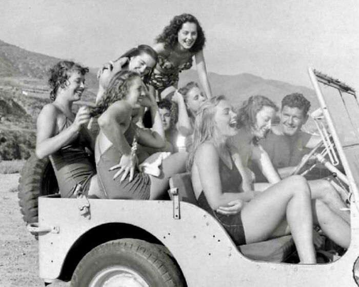 Group of people enjoying a ride in an open jeep on a sunny day, showcasing rare historical fun in leisure time.