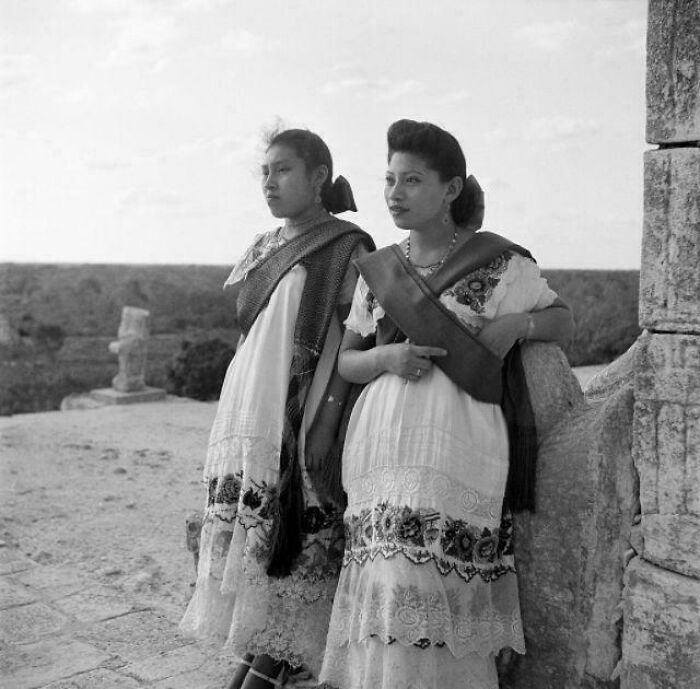 Two women in traditional clothing on a stone structure, showcasing rare historical cultural attire.