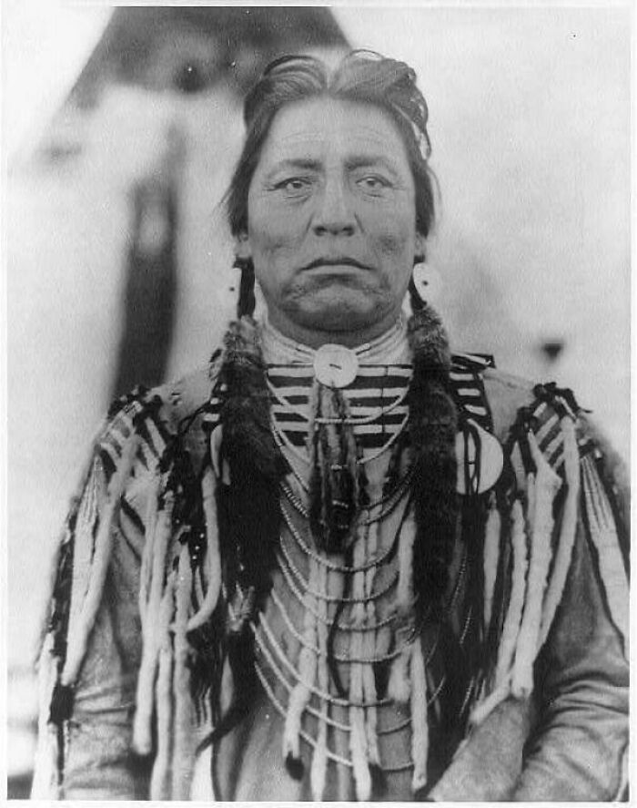 A historical photo of a Native American man wearing traditional attire with intricate beadwork and feathers.