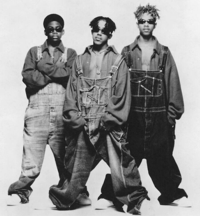 '90s music group in baggy denim overalls and sunglasses, embodying classic '90s fashion trends.