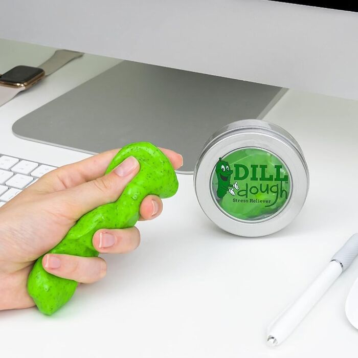 Person squeezing green stress reliever labeled "DILL dough," a funny Valentine's Day gift near a computer.