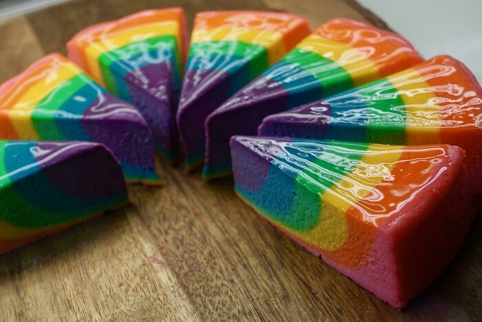 Rainbow cake slices on a wooden board, showcasing vibrant layers. Interesting Japan Pics highlight delightful desserts.