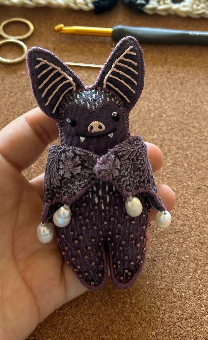 Hand holding a small embroidered bat with detailed stitching and decorative pearls showcasing embroidery skills.