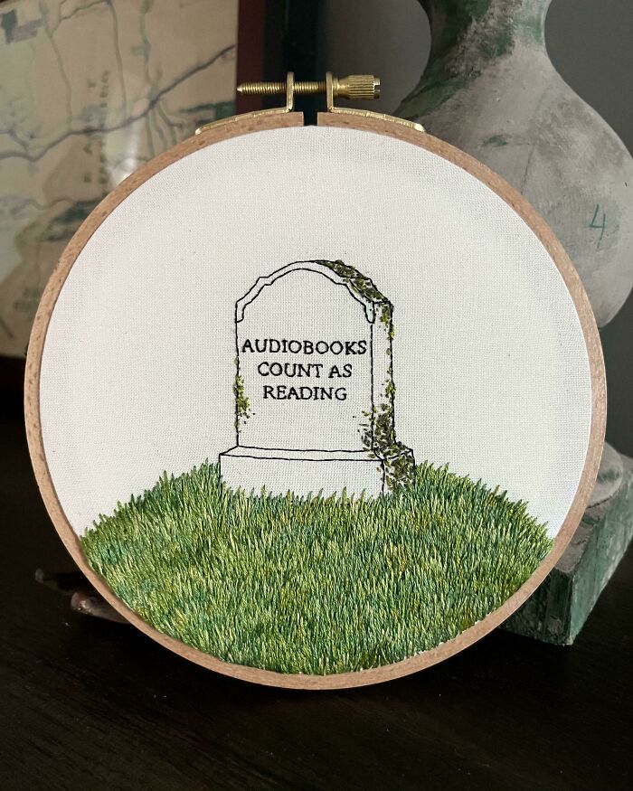 Embroidery hoop featuring detailed grass and a tombstone stitched with the phrase audiobooks count as reading.