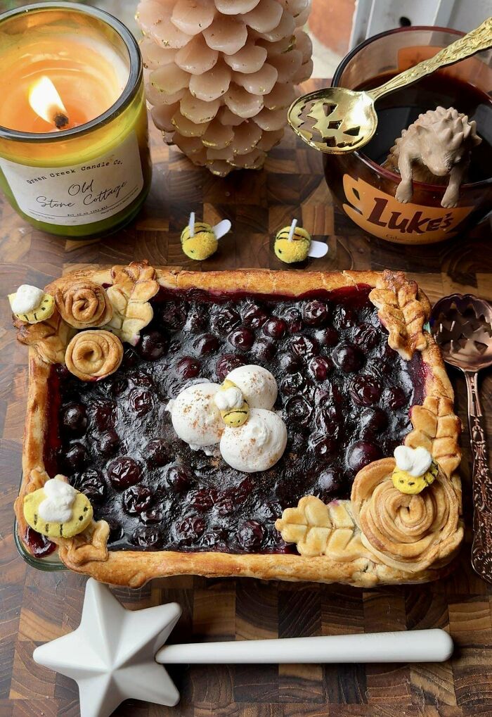Blueberry bake with decorative bee accents and leaf crust details, surrounded by cozy candlelight and festive tableware.