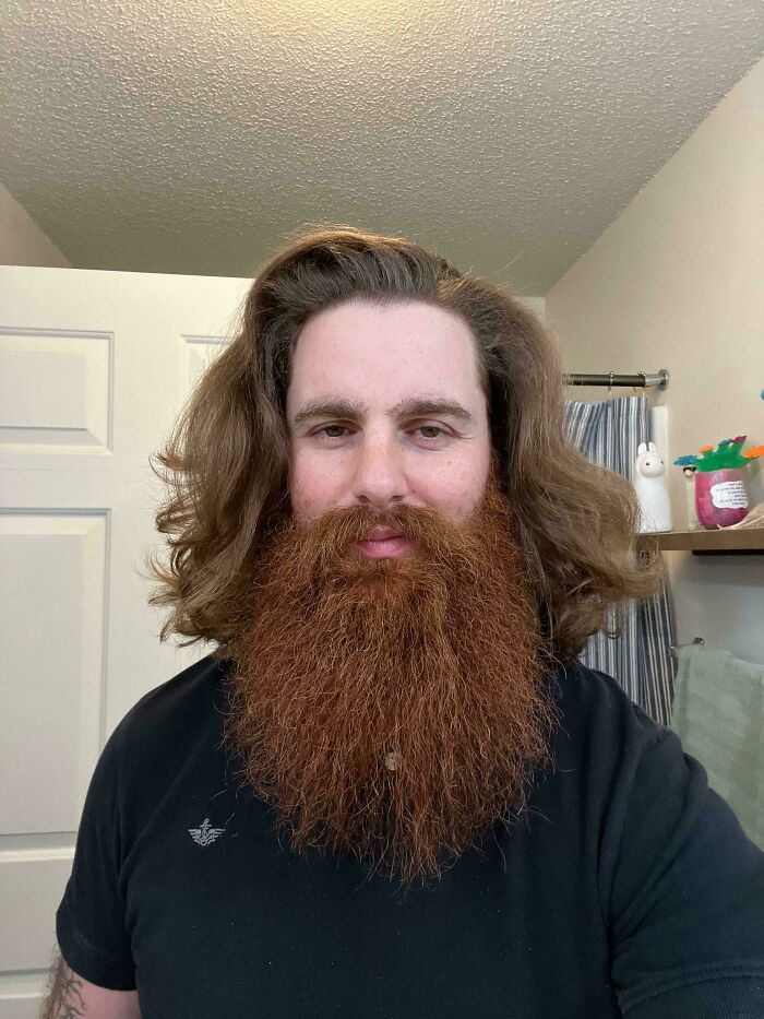 Man with fierceflow beautiful hair and long thick red beard wearing a black shirt indoors in a bathroom.