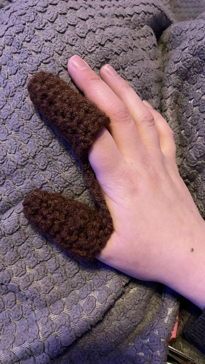 Hand wearing unique brown crochet finger covers resting on textured gray fabric, showcasing crochet masterpieces craftsmanship.